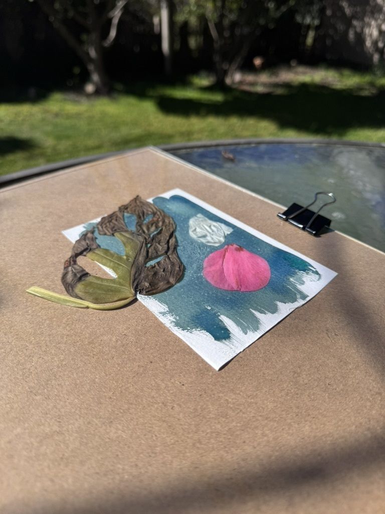 A card with a a pink flower and a white garlic skin on a brown surface.