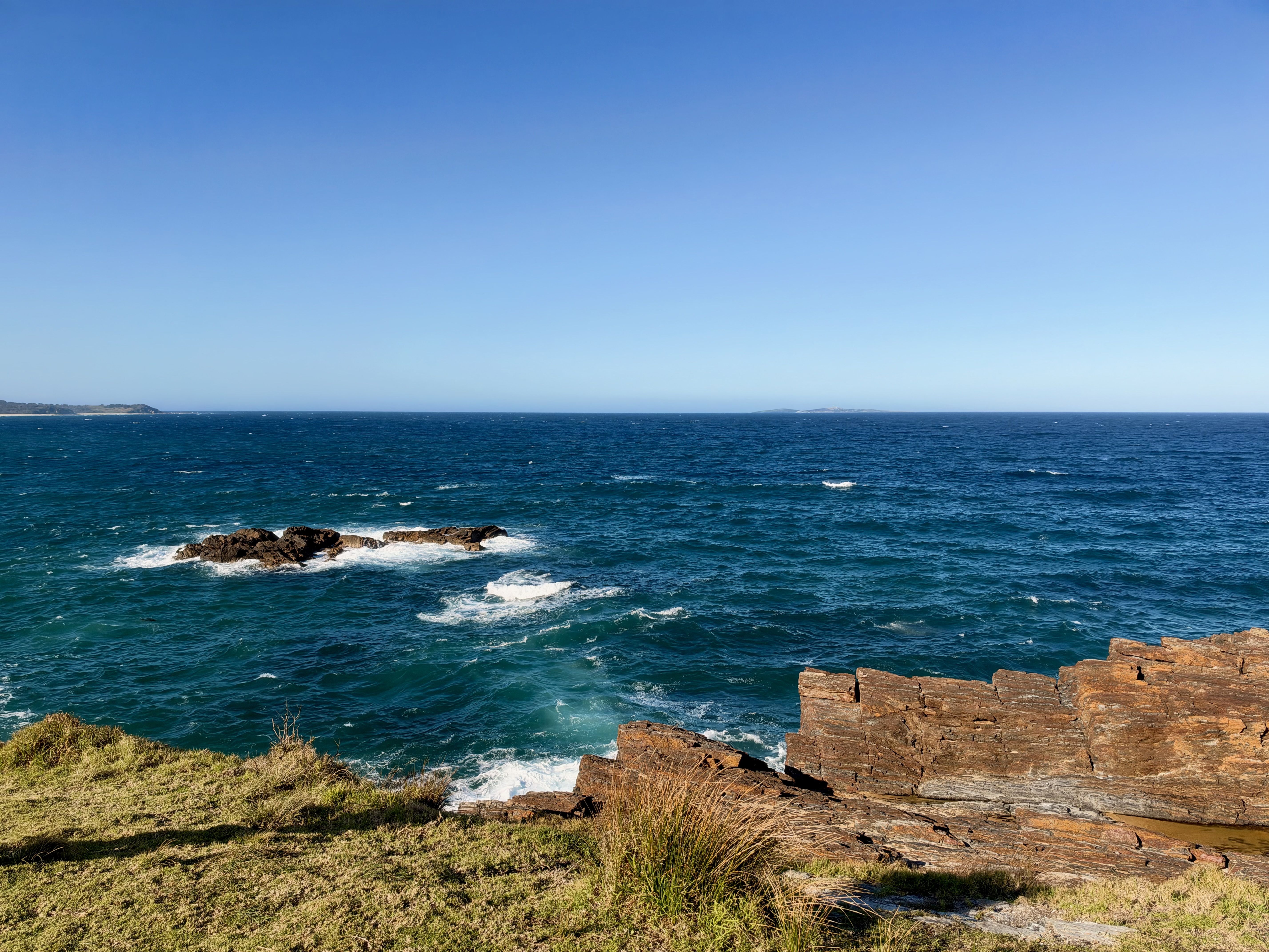 Blue ocean with waves crashing against rocky shore under clear sky.