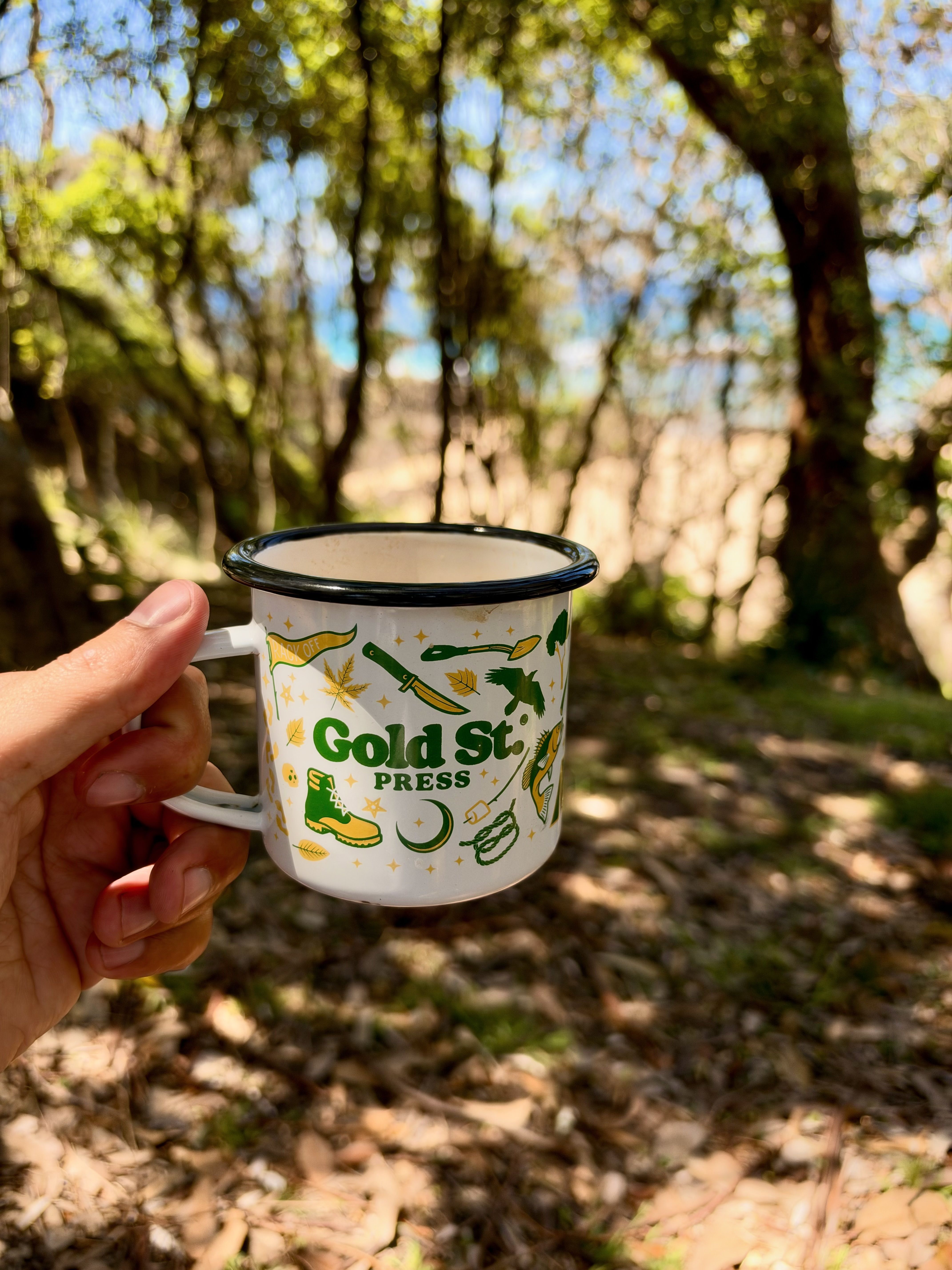 A hand holds a white mug with green text and illustrations in a forest setting.