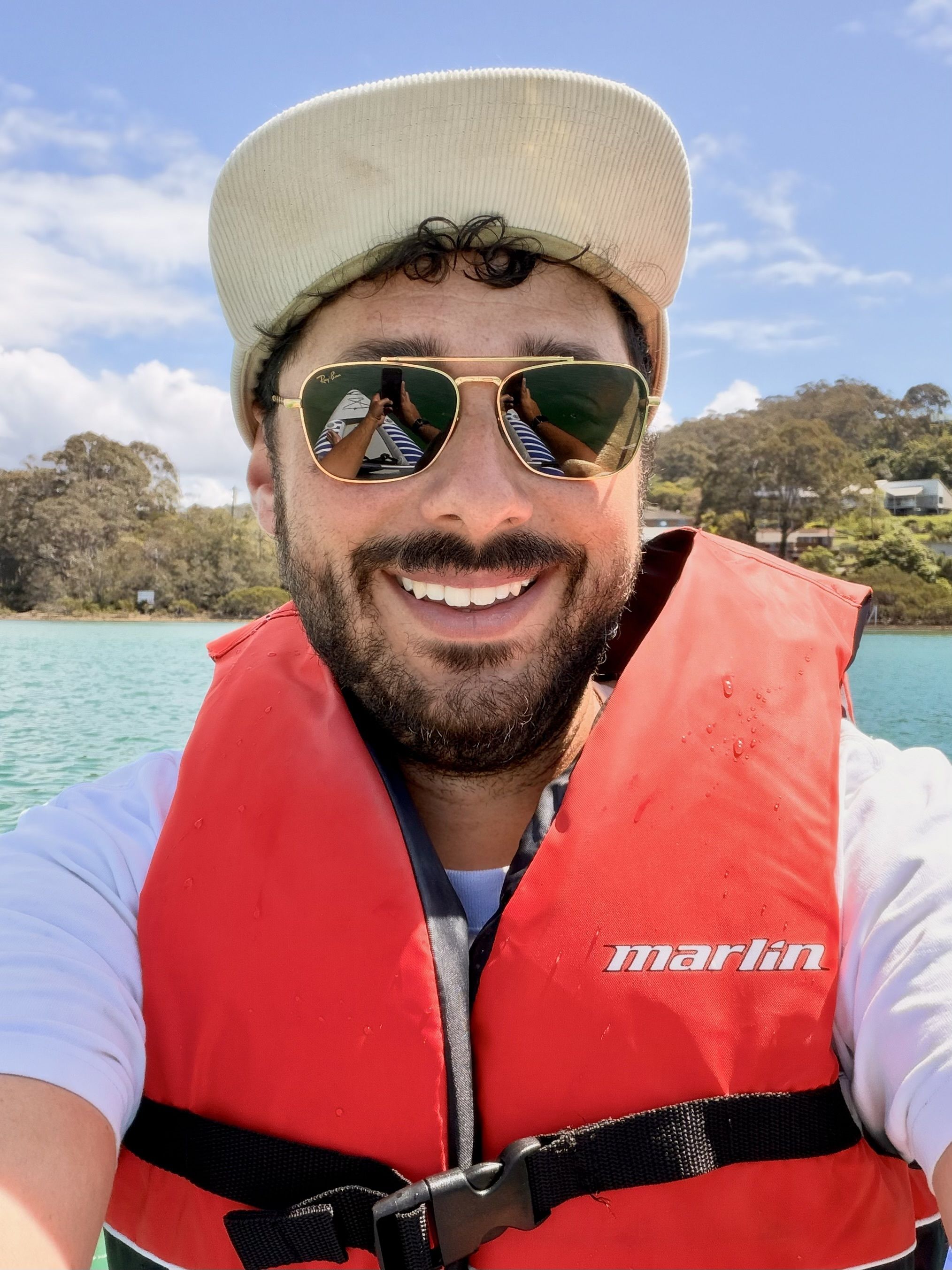 A man wearing a red life vest and a hat posing for a photo on a body of water.