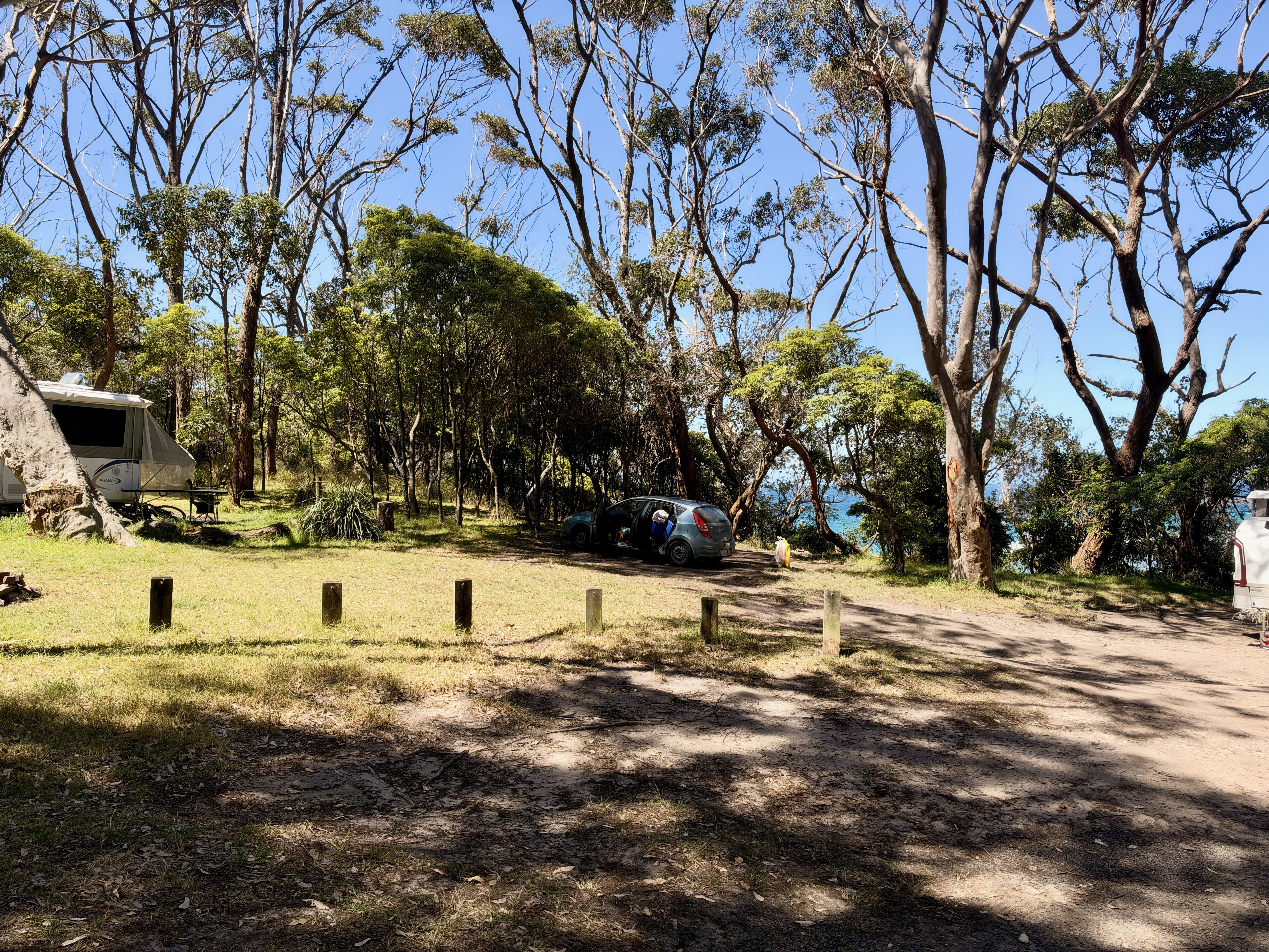 A campsite with a tent, a car, and trees under a clear blue sky.