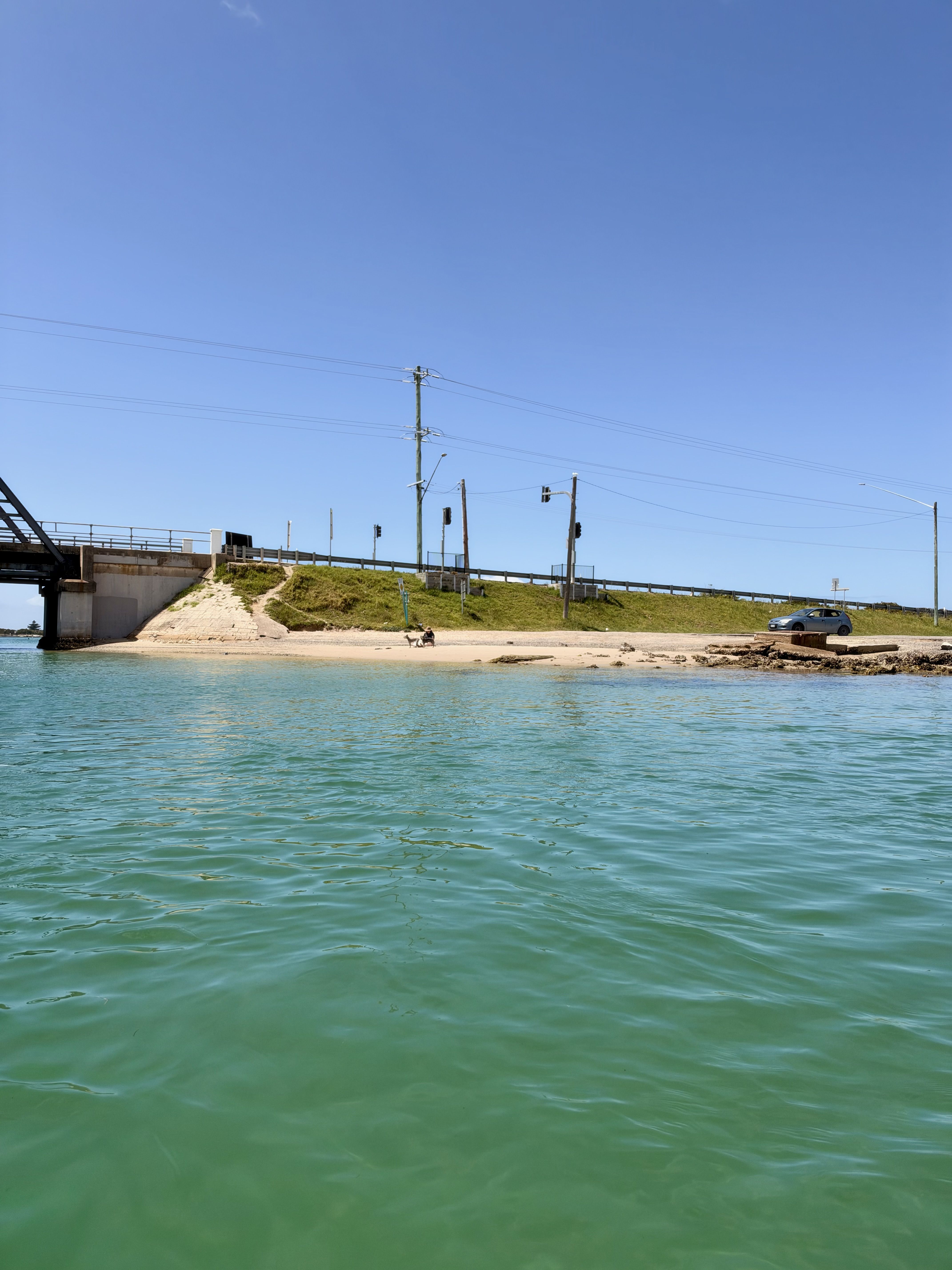 A body of water with a bridge, grassy area, and a vehicle under a clear sky.