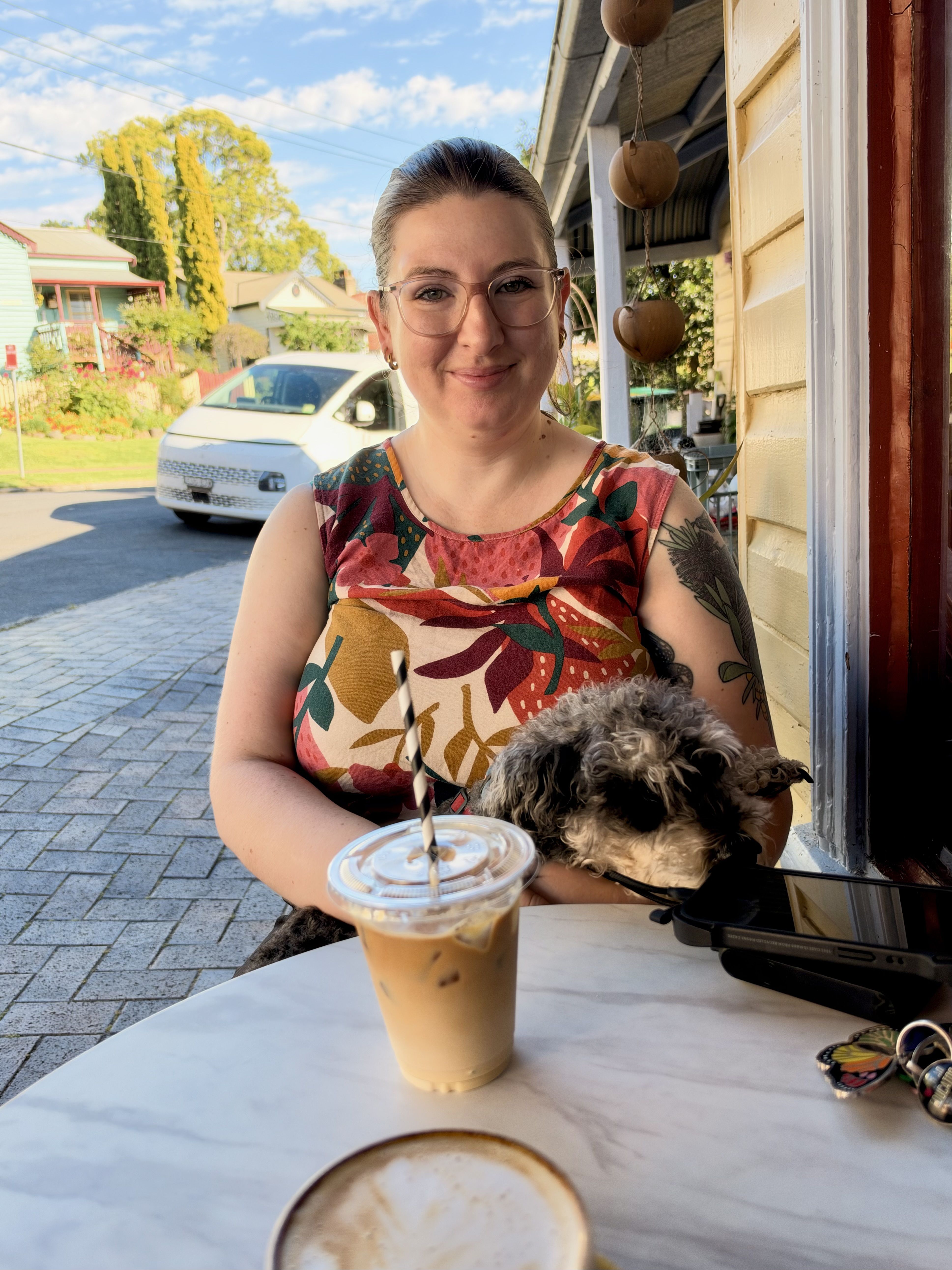 A woman with a dog on her lap sits at a table with a drink.