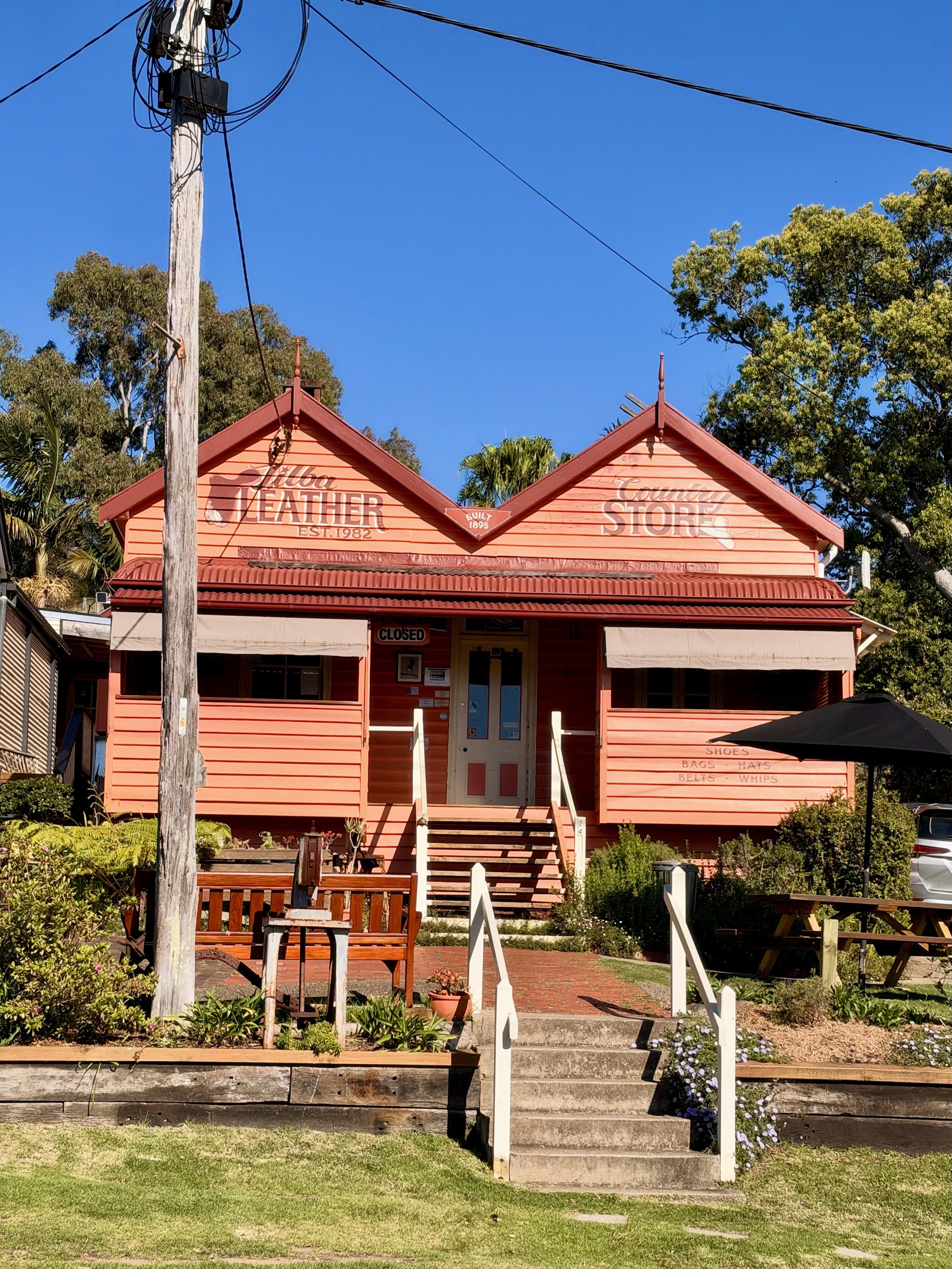 Red wooden building with a sign, bench, and a tree.