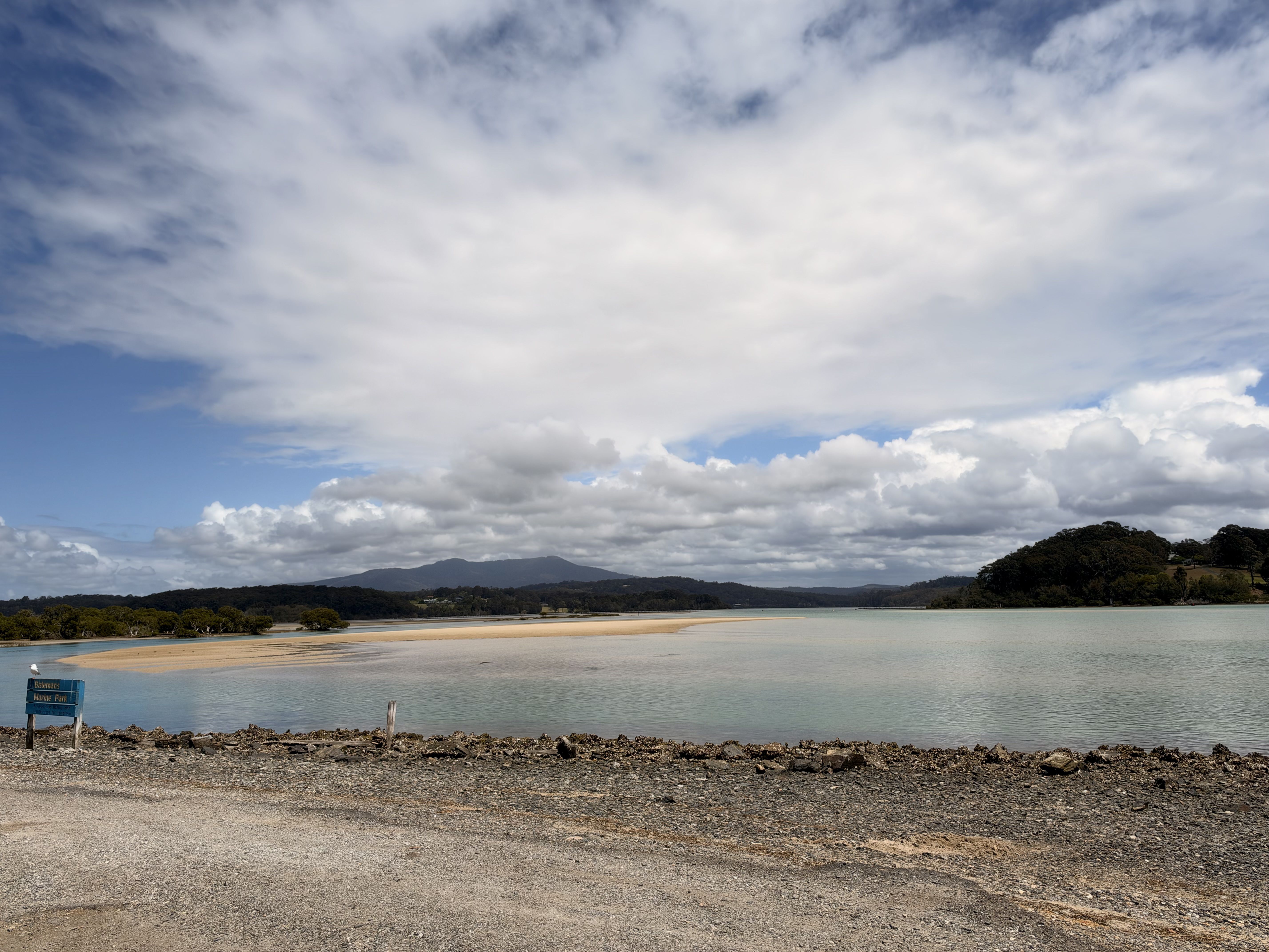 A rocky shore with a body of water, a sandy beach, and a cloudy sky.