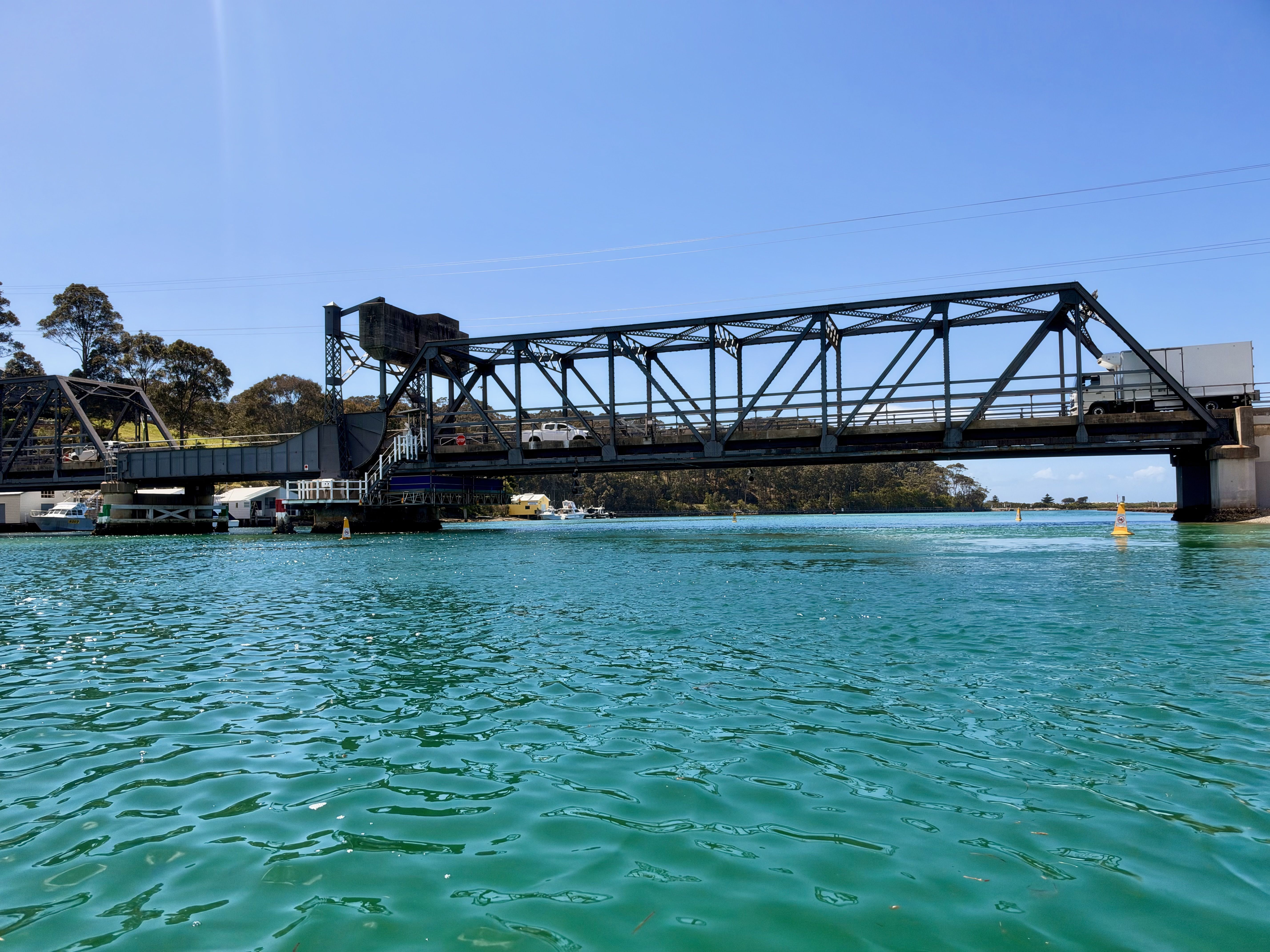 A metal bridge over turquoise water under a clear blue sky.