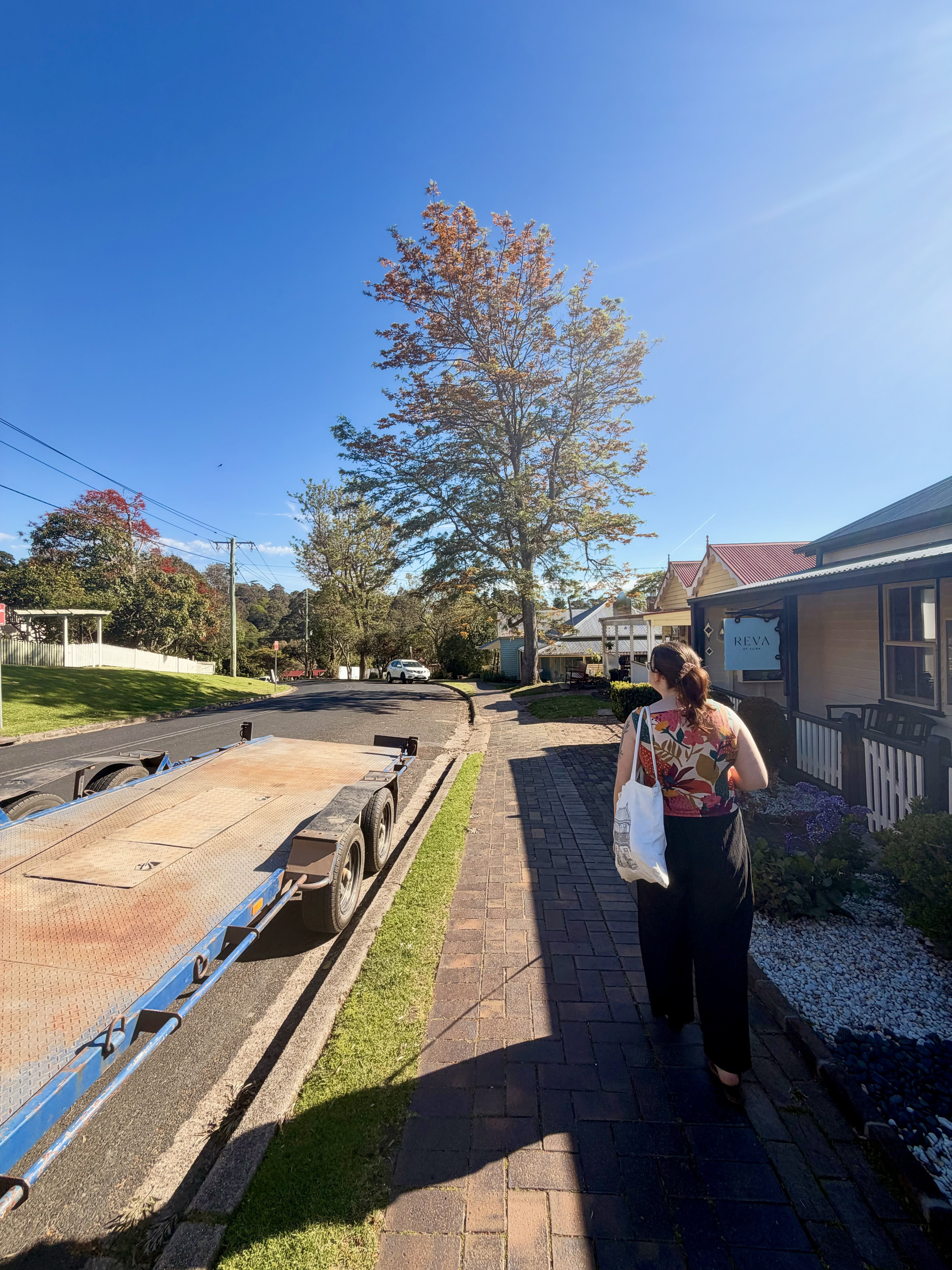 A woman carrying a bag walks on a brick path near a building.