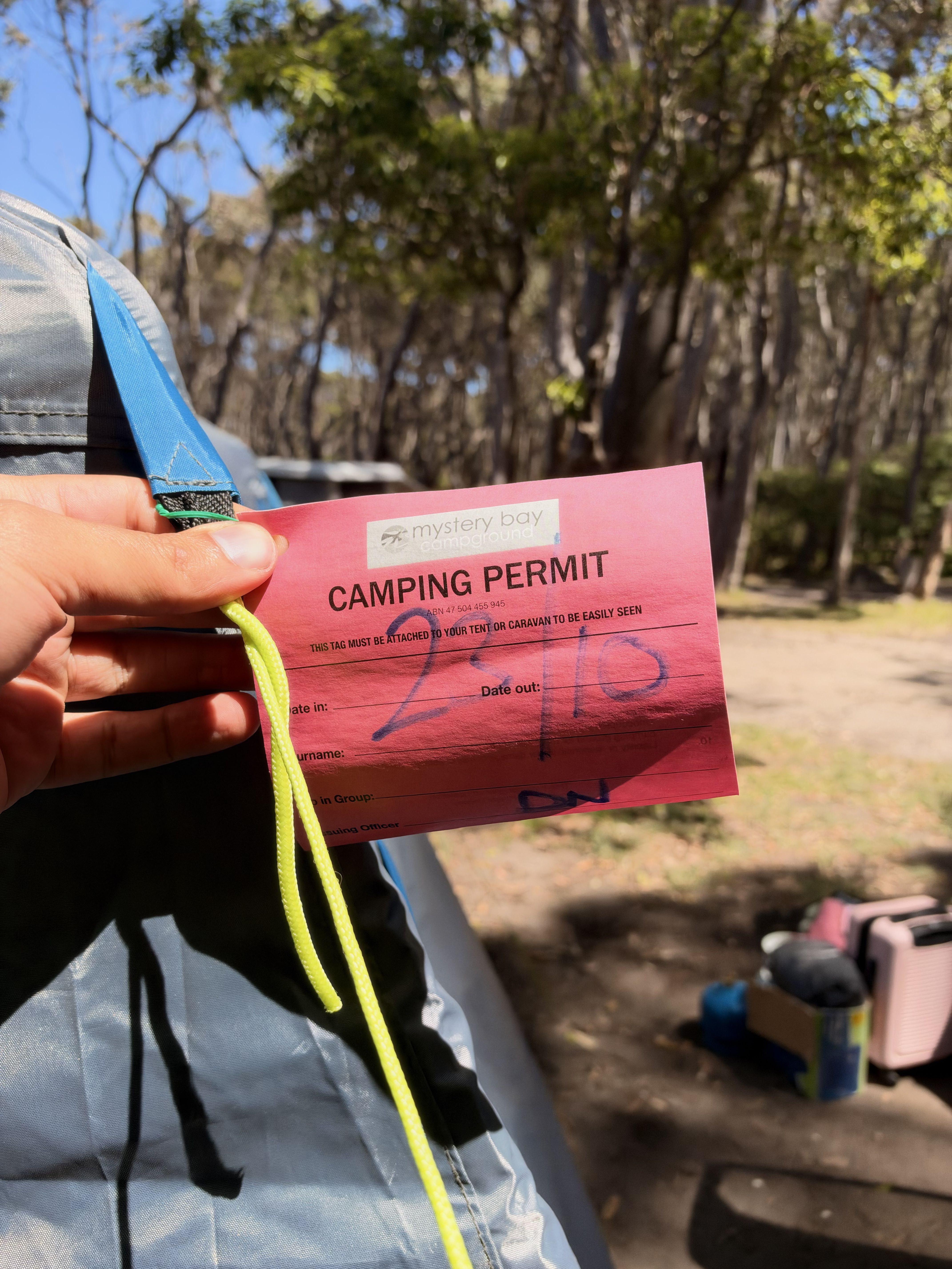 A person holds a red camping permit with a yellow lanyard in a wooded area.