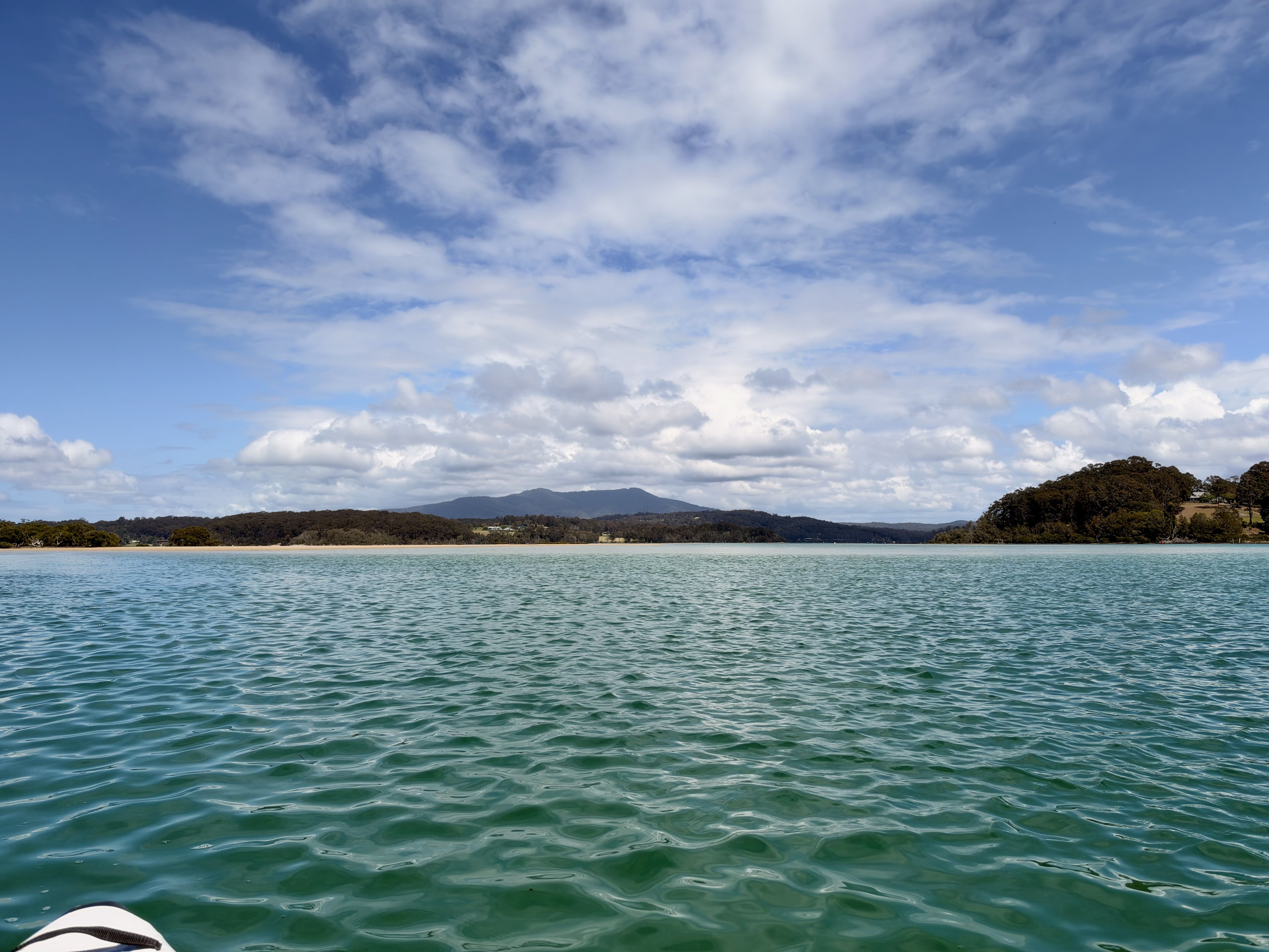 Blue water with a distant mountain and clouds under a blue sky.
